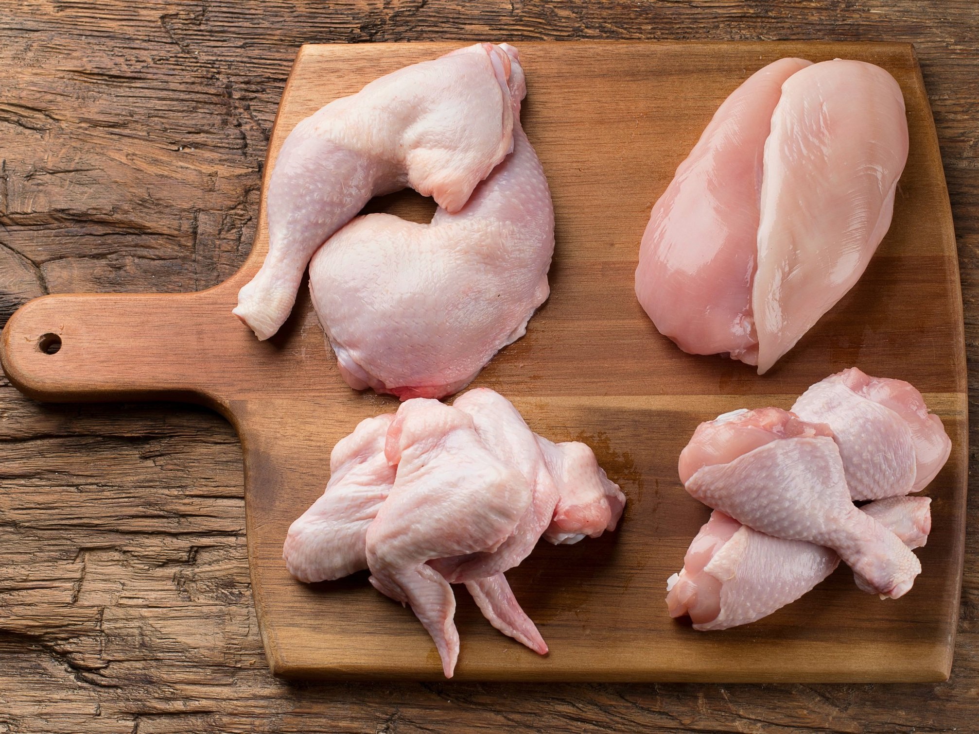 Raw chicken pieces including thighs, breasts, and wings arranged on a wooden cutting board, showcasing various cuts for cooking and meal preparation.