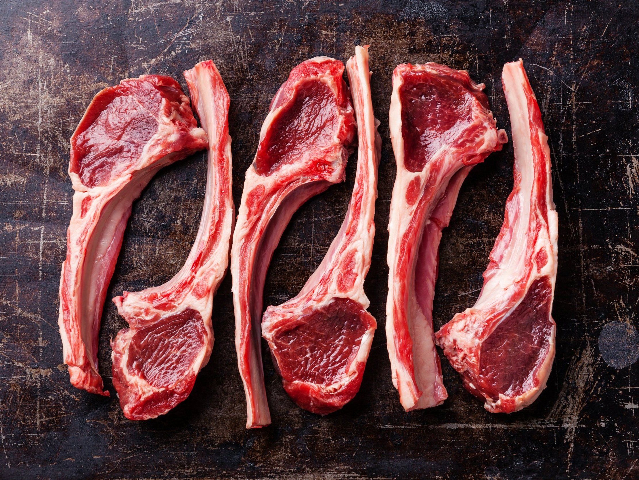 Raw lamb chops arranged neatly on a rustic wooden cutting board, showcasing their rich red color and marbling, ideal for grilling or roasting.